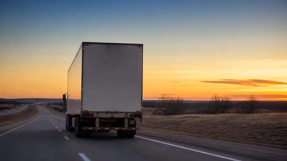 A semi truck on an interstate across open plains at dusk